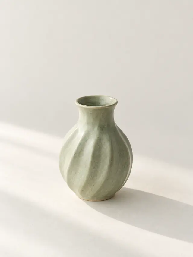 Pale green ceramic vase on an off-white surface; original AI illustration, not a workspace result